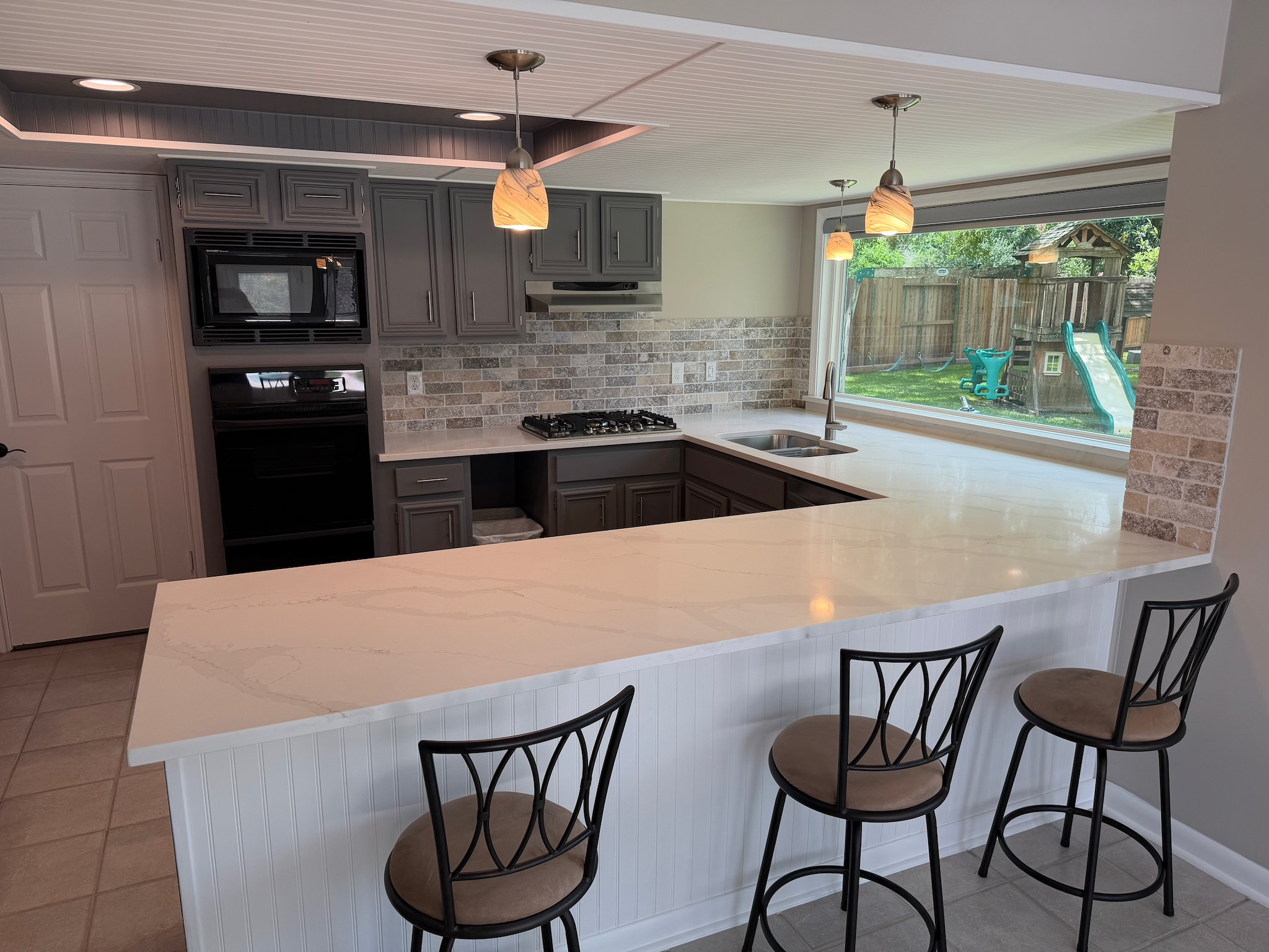 2326 Streamcrest Lane Sugar Land, TX 77479 - Photo 10 of 42 Kitchen with tile flooring, Quartz Counters, tile backsplash, gas oven & cooktop. Beadboard ceiling. Pendant lights. View of backyard and pool area.