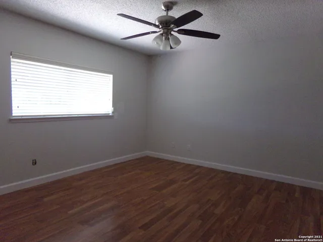 an empty room with wooden floor ceiling fan and windows