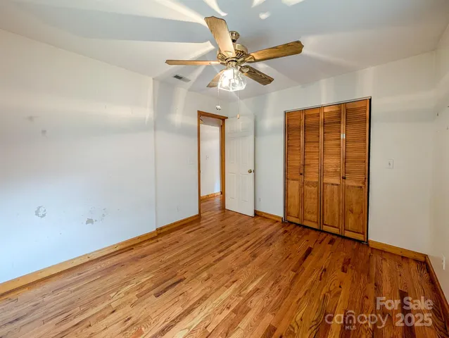 a view of an empty room with wooden floor and a ceiling fan