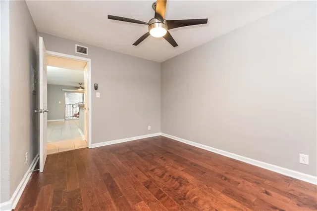 an empty room with wooden floor ceiling fan and windows