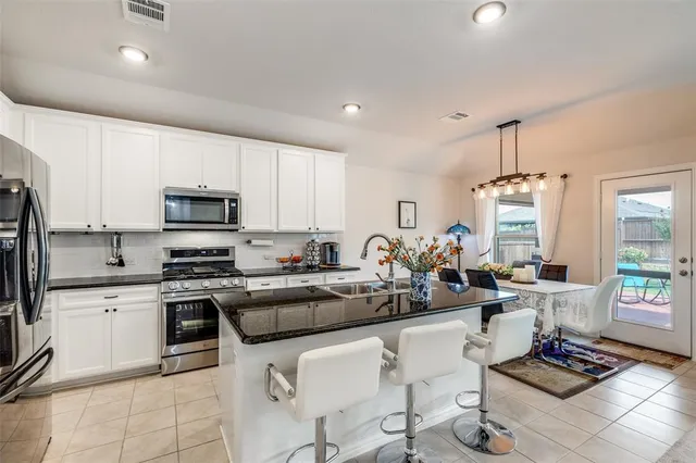 a kitchen with stainless steel appliances a stove a sink a refrigerator white cabinets and a dining table with wooden floor