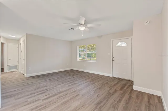an empty room with wooden floor a ceiling fan and windows