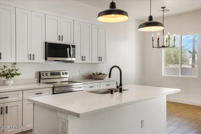 a kitchen with a sink a chandelier stainless steel appliances and cabinets