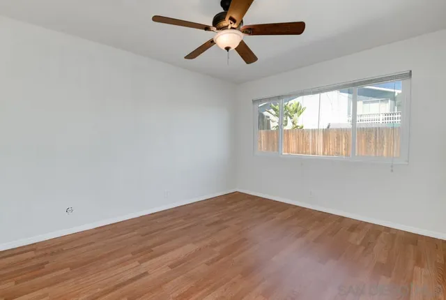 an empty room with wooden floor and a ceiling fan