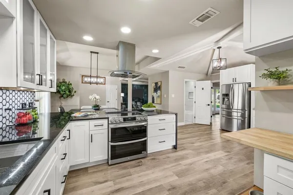 a kitchen with stainless steel appliances kitchen island granite countertop a stove top oven a sink a refrigerator and white cabinets