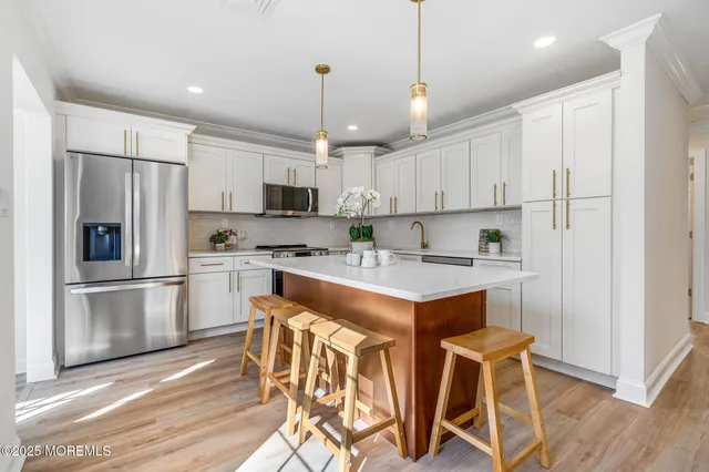 a kitchen with stainless steel appliances granite countertop a refrigerator a sink dishwasher a stove and white cabinets with wooden floor