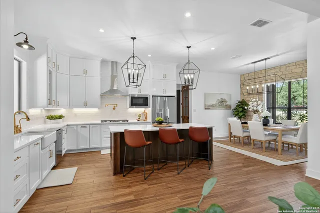 a kitchen with stainless steel appliances a dining table a sink a stove a refrigerator cabinets and wooden floor