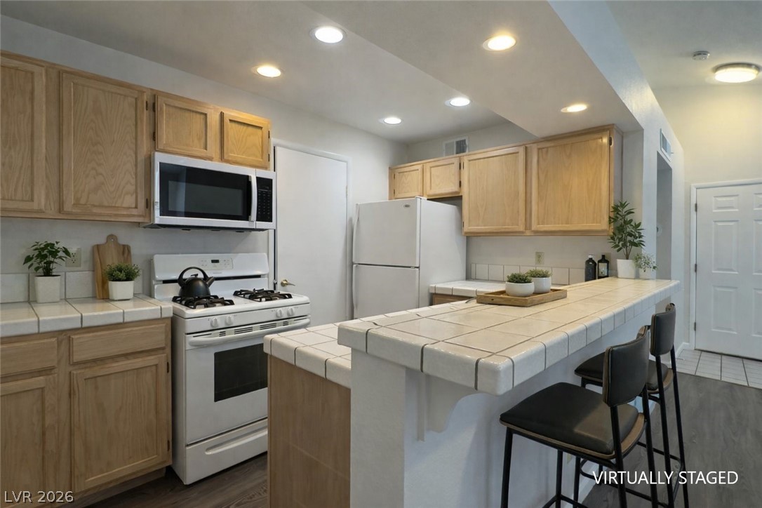 7570 West Flamingo Road, Unit 209 Las Vegas, NV 89147 - Photo 10 of 30 Kitchen featuring tile countertops, white appliances, a breakfast bar, light wood finish cabinets, and dark wood-type flooring