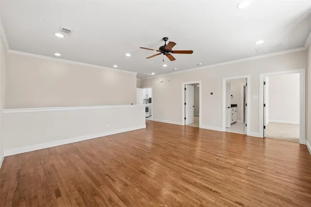 a view of an empty room with wooden floor and a ceiling fan