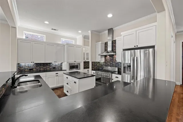 a kitchen with stainless steel appliances a stove a sink a refrigerator white cabinets and wooden floor