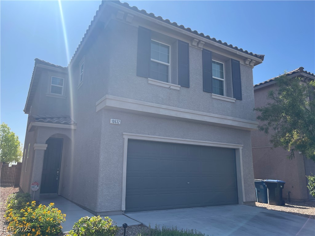 Traditional-style home featuring stucco siding, a tiled roof, an attached garage, and driveway
