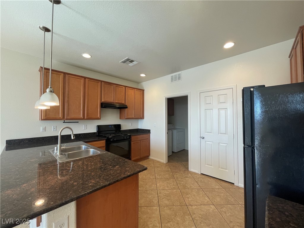 10632 Summerbell Street Las Vegas, NV 89179 - Photo 6 of 16 Kitchen with black appliances, under cabinet range hood, washer and dryer, brown cabinets, and a peninsula
