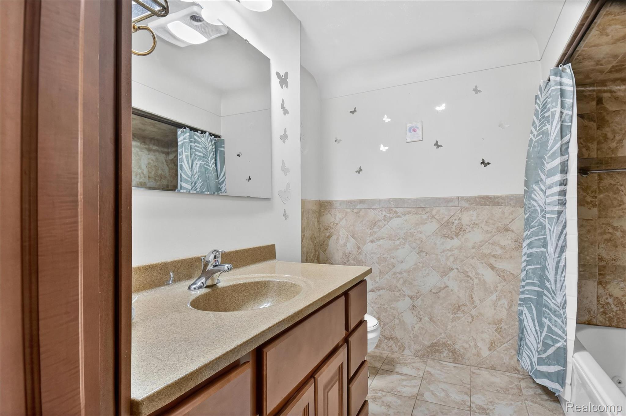 3949 West Burns Line Road Brown City, MI 48416 - Photo 35 of 70 Bathroom featuring a wood-finish vanity with an integrated sink and a light-toned countertop, a large wall-mounted mirror, and a shower-over-tub combination with full-height tile surround