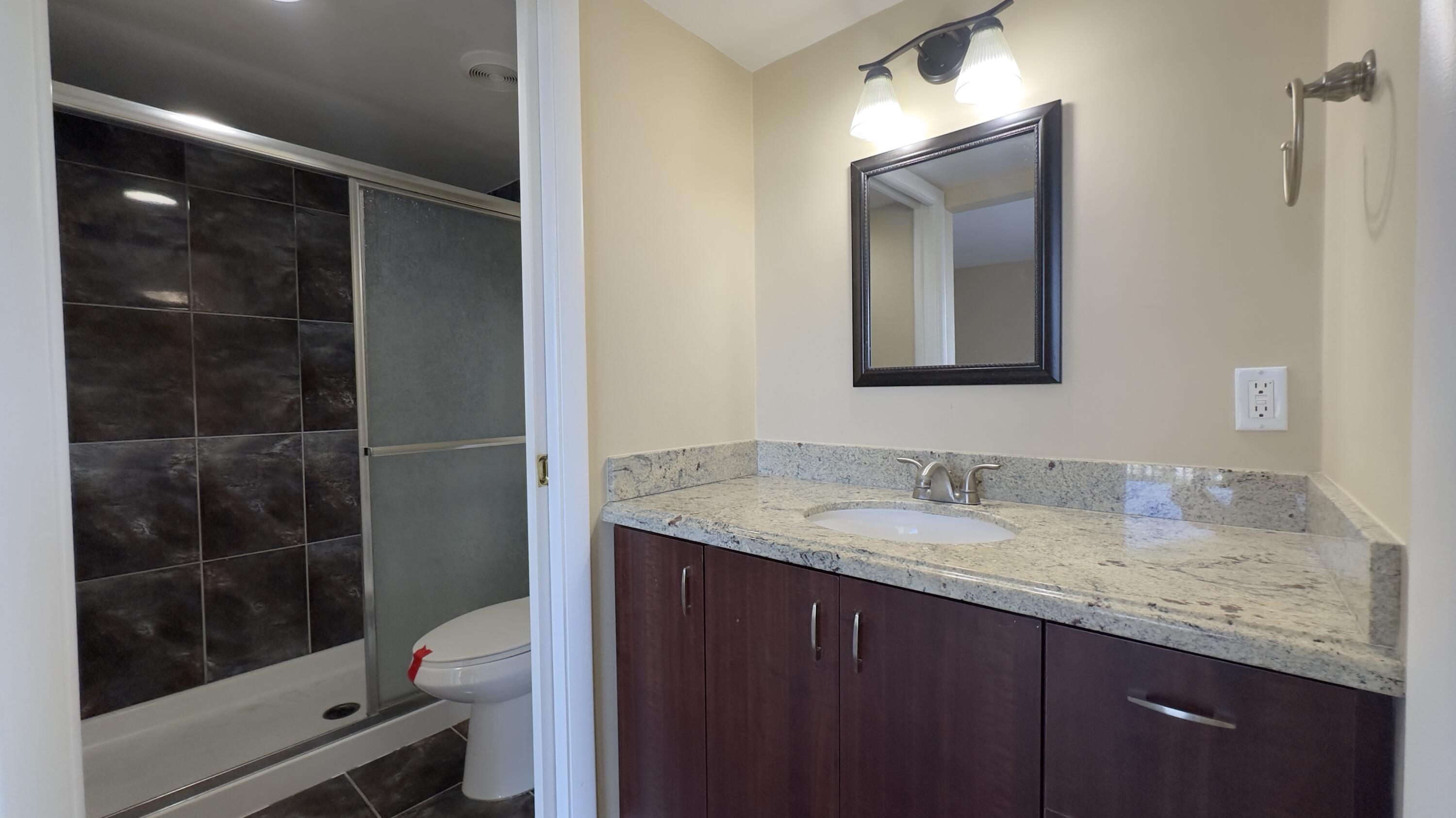 2425 Presidential Way, Unit 203 West Palm Beach, FL 33401 - Photo 14 of 35 a bathroom with a granite countertop sink a mirror and a shower