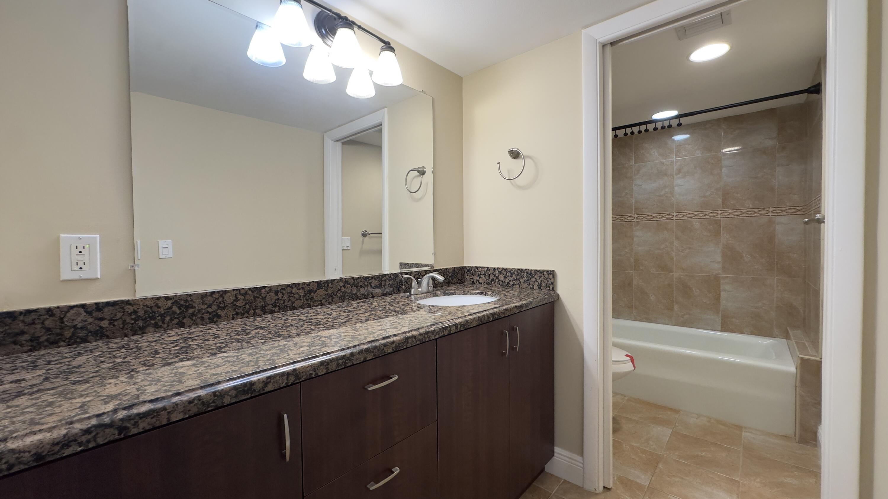 2425 Presidential Way, Unit 203 West Palm Beach, FL 33401 - Photo 15 of 35 a bathroom with a granite countertop sink a toilet and shower