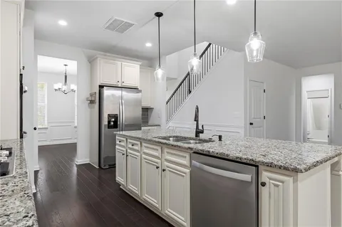 a kitchen with stainless steel appliances granite countertop a sink a refrigerator and a wooden floor