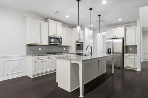 a kitchen with stainless steel appliances granite countertop a sink a stove a refrigerator and white cabinets