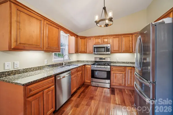 a kitchen with stainless steel appliances granite countertop a stove top oven a sink dishwasher and a refrigerator with wooden floor