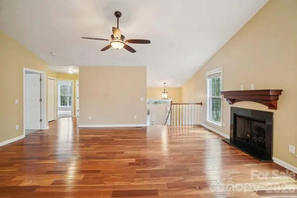 a view of an empty room with wooden floor fireplace and a window