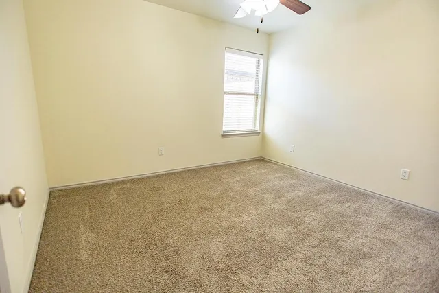 an empty room with a chandelier fan and windows