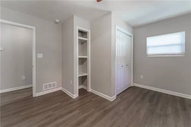 an empty room with wooden floor closet and windows