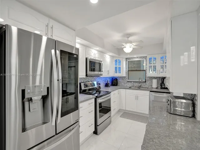 a kitchen with stainless steel appliances granite countertop a refrigerator a stove a sink and white cabinets with wooden floor