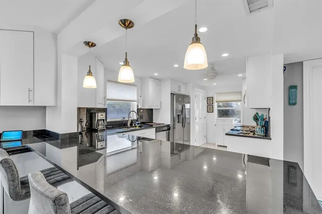 a kitchen with stainless steel appliances granite countertop a stove top oven a sink a dining table and chairs with white cabinets