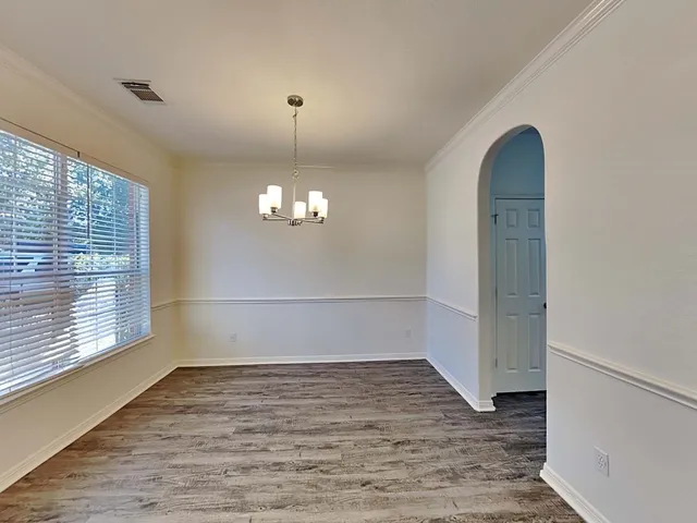 an empty room with wooden floor chandelier and windows