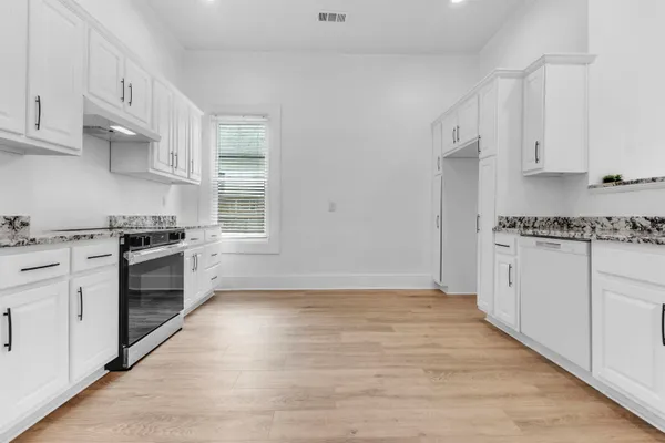 a kitchen with granite countertop a stove cabinets and wooden floor