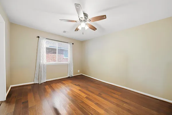 an empty room with wooden floor fan and windows