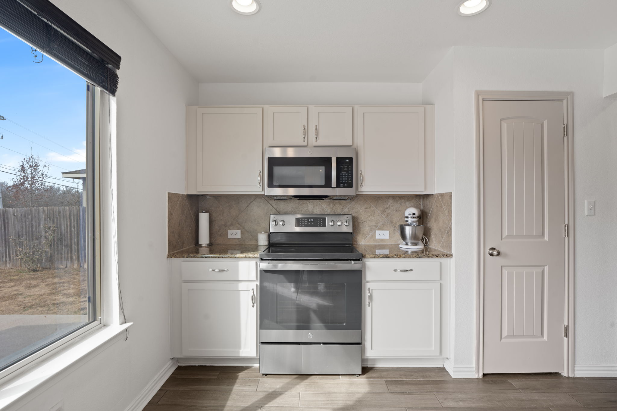 13109 Pealing Way Manor, TX 78653 - Photo 12 of 32 Kitchen featuring light stone countertops, stainless steel appliances, decorative backsplash, light wood-style floors, and white cabinets