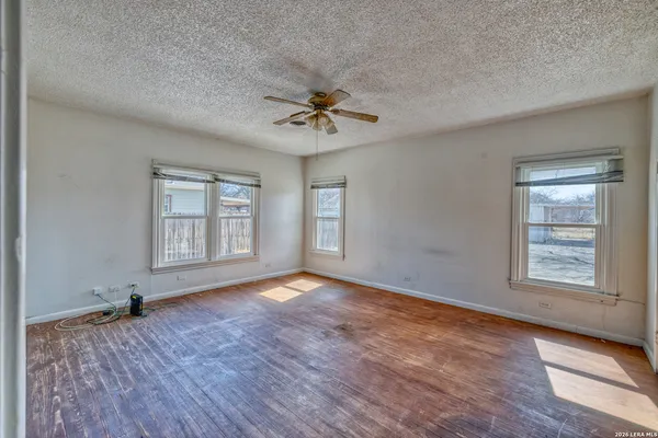 an empty room with wooden floor chandelier fan and windows