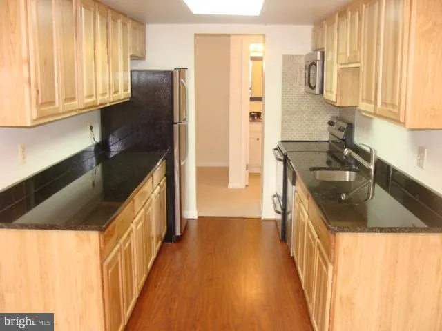 a kitchen with granite countertop a sink a refrigerator and wooden cabinets