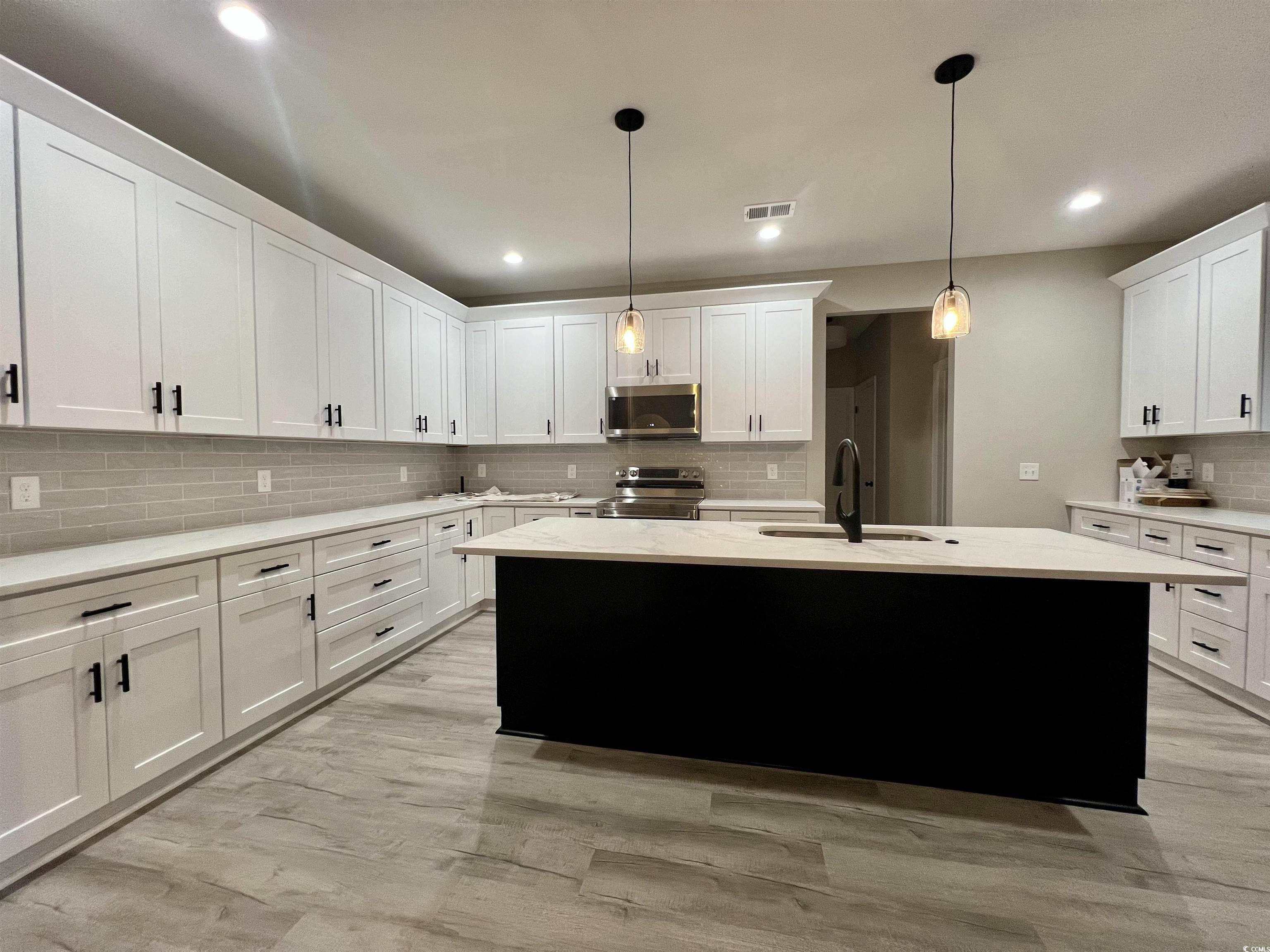 1107 Highway 9 Business Loris, SC 29569 - Photo 15 of 33 Kitchen with a kitchen island with sink, white cabinets, hanging light fixtures, sink, and appliances with stainless steel finishes