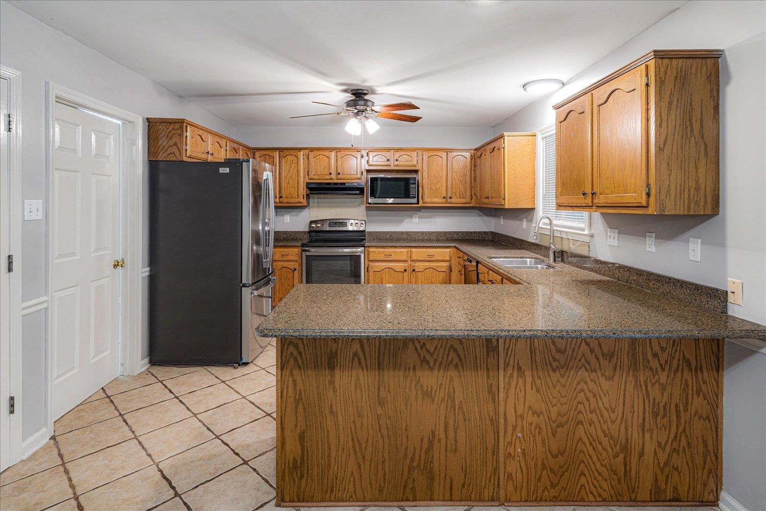 910 Sugar Cove Collierville, TN 38017 - Photo 12 of 32 Kitchen with stainless steel appliances, a peninsula, brown cabinets, dark stone countertops, and light tile patterned flooring