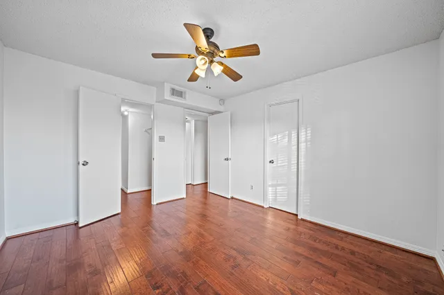 a view of an empty room with wooden floor and a ceiling fan