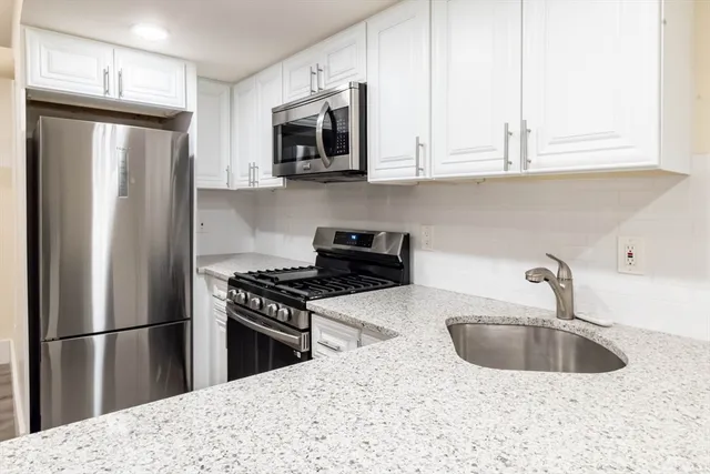 a kitchen with stainless steel appliances granite countertop a refrigerator a sink a stove a microwave and white cabinets