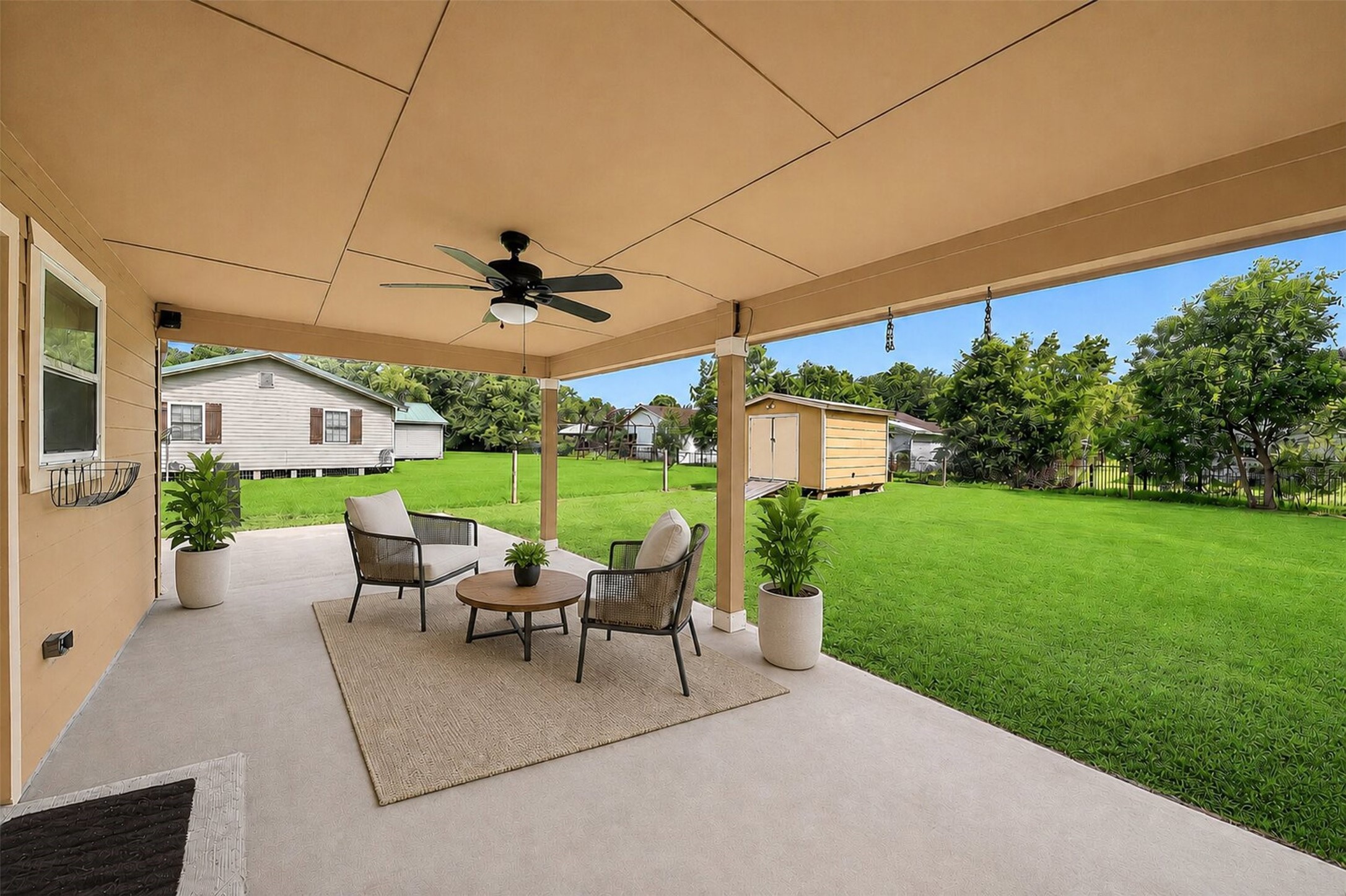 148 Fear Road Winnie, TX 77665 - Photo 23 of 34 This photo showcases a spacious covered patio with a ceiling fan and seating area, overlooking a large, well-maintained backyard with a storage shed and lush greenery, perfect for outdoor relaxation and entertainment. This photo is virtually staged.