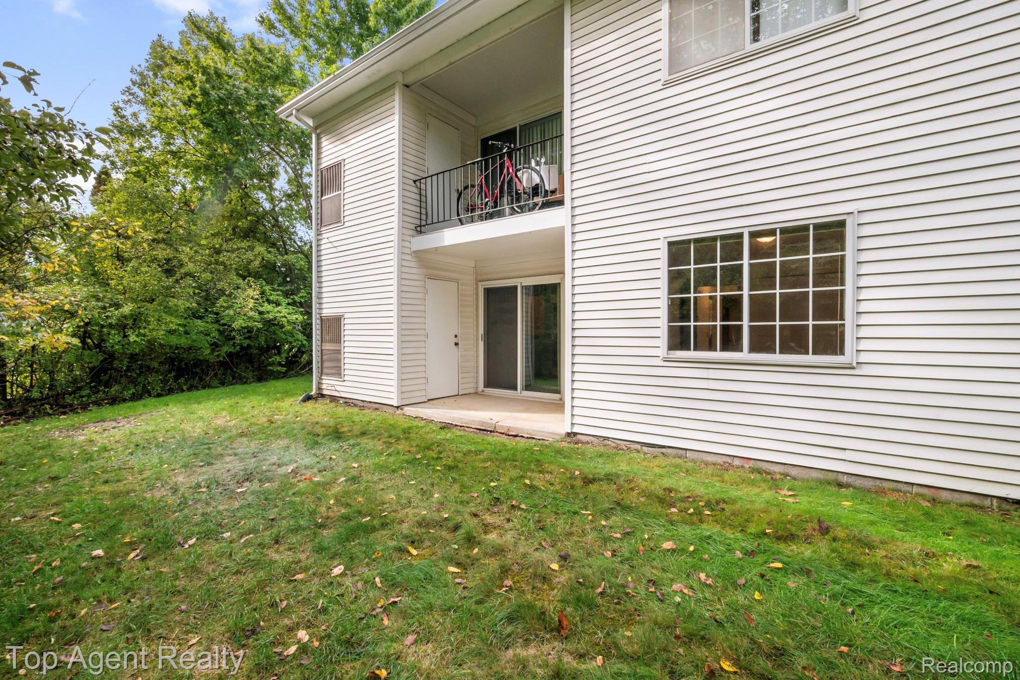 23420 Middlebelt Road Farmington, MI 48336 - Photo 27 of 32 White horizontal siding exterior with a ground-level patio and an upper-level balcony featuring a metal railing