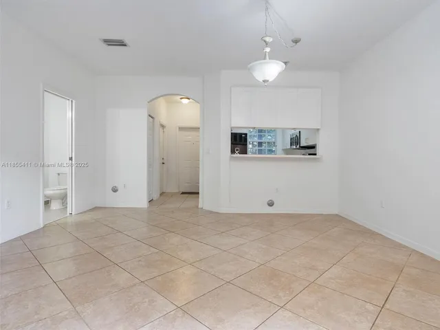 an empty room with a chandelier fan and kitchen view
