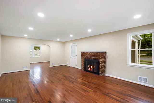 an empty room with wooden floor fireplace and windows