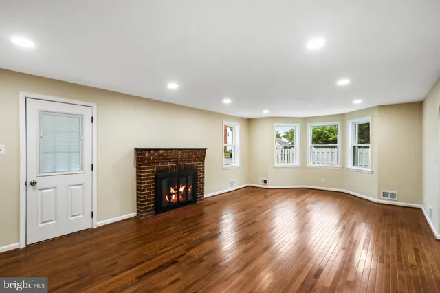 a view of an empty room with wooden floor fireplace and a window