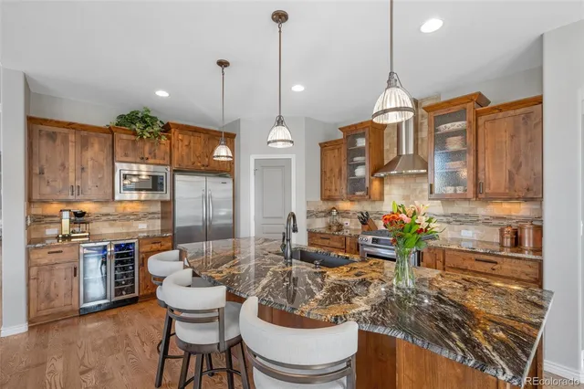 a kitchen with stainless steel appliances granite countertop a stove a sink a refrigerator a dining table and chairs with the wooden floor