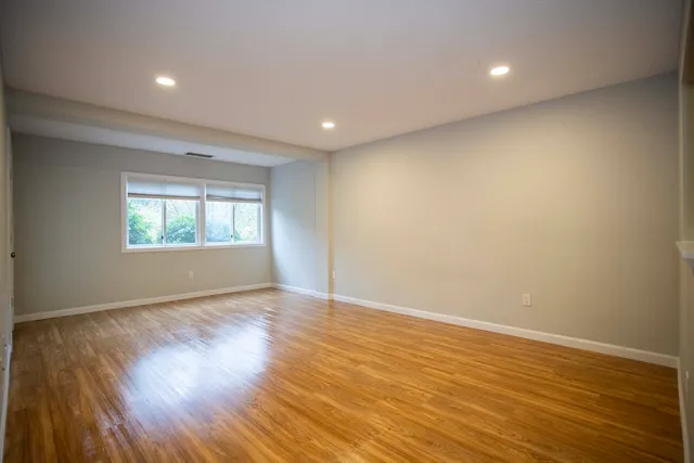 a view of an empty room with wooden floor and a window