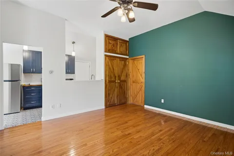 an empty room with wooden floor and way to kitchen