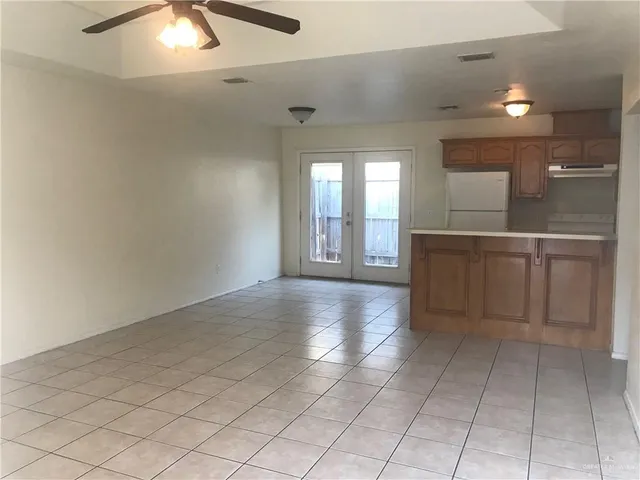 an empty room with kitchen and chandelier fan
