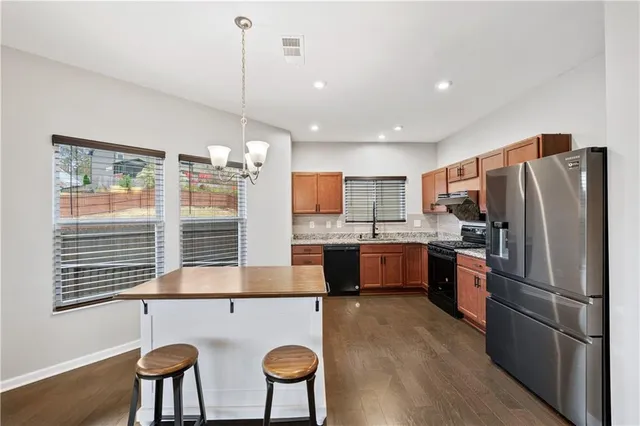 a kitchen with stainless steel appliances granite countertop a refrigerator a sink dishwasher a stove and a dining table with wooden floor