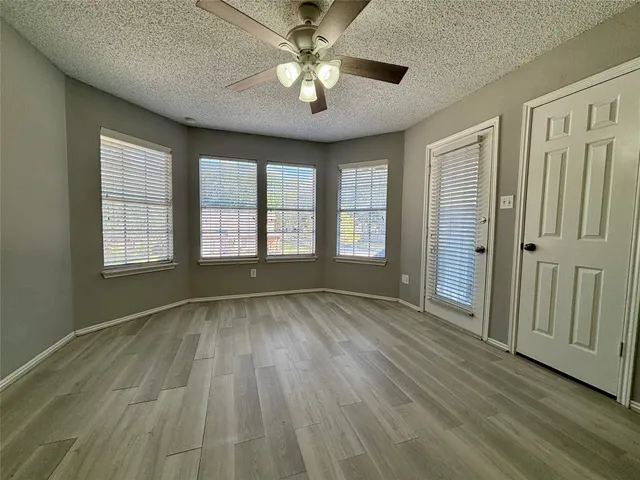 an empty room with wooden floor chandelier fan and windows