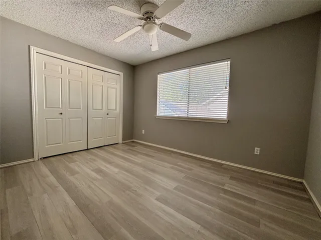 an empty room with wooden floor fan and windows