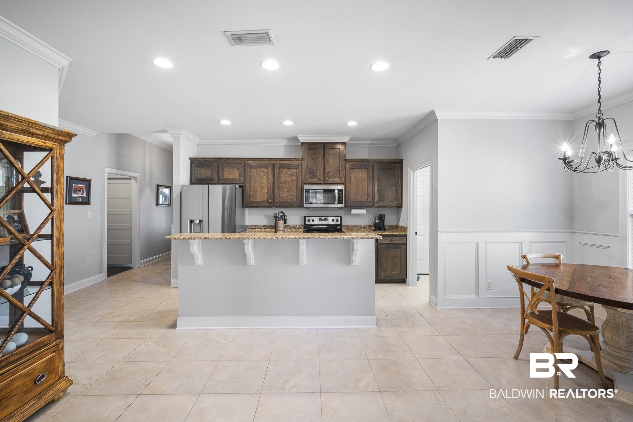 8594 Rosedown Lane Daphne, AL 36526 - Photo 6 of 30 Kitchen with a breakfast bar, stone countertops, stained cabinetry, a kitchen island with sink, and crown molding